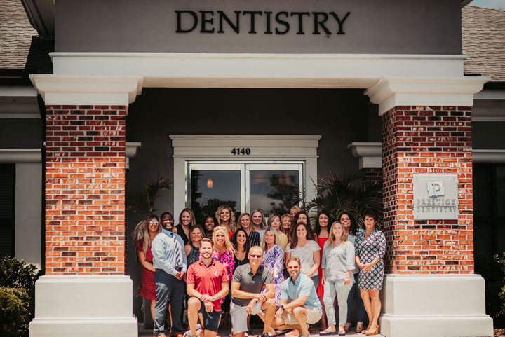 The image shows a group of people posing outside a dental clinic named  Dentistry .
