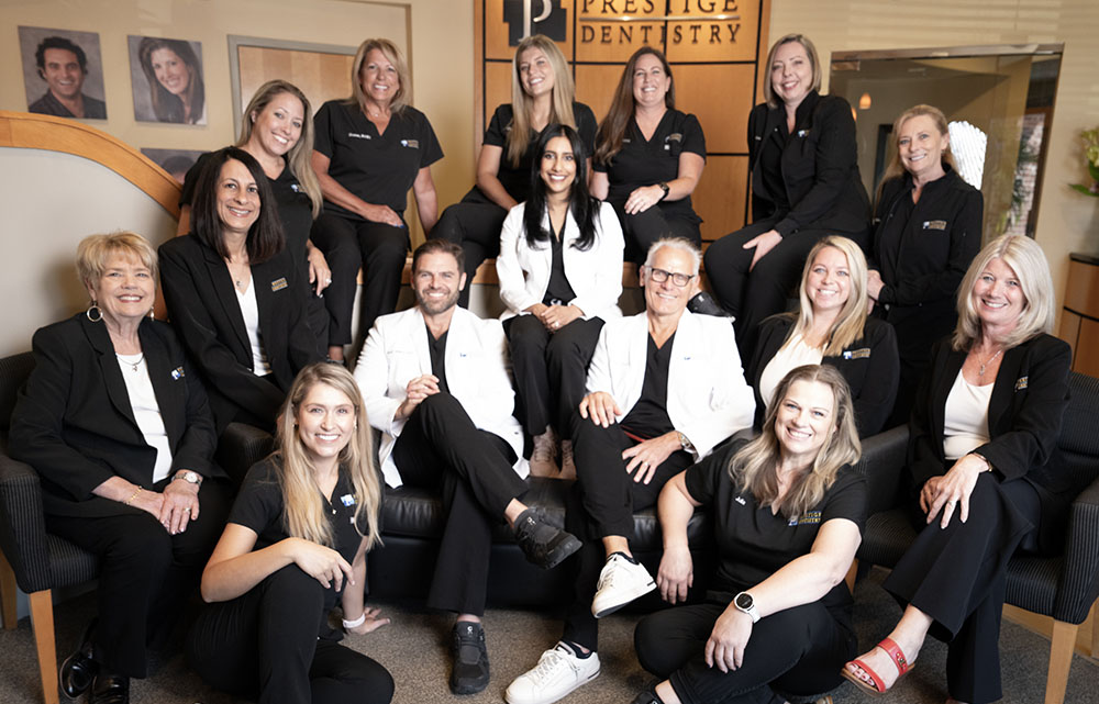 The image shows a group of individuals posing together, likely for a professional purpose, such as a dental practice team photo. They are all dressed in uniforms, suggesting they work in a medical field, specifically dentistry.