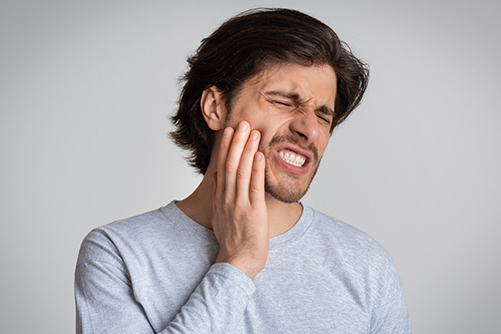 The image shows a man with a surprised expression, holding his hand over his mouth, possibly indicating pain or discomfort.