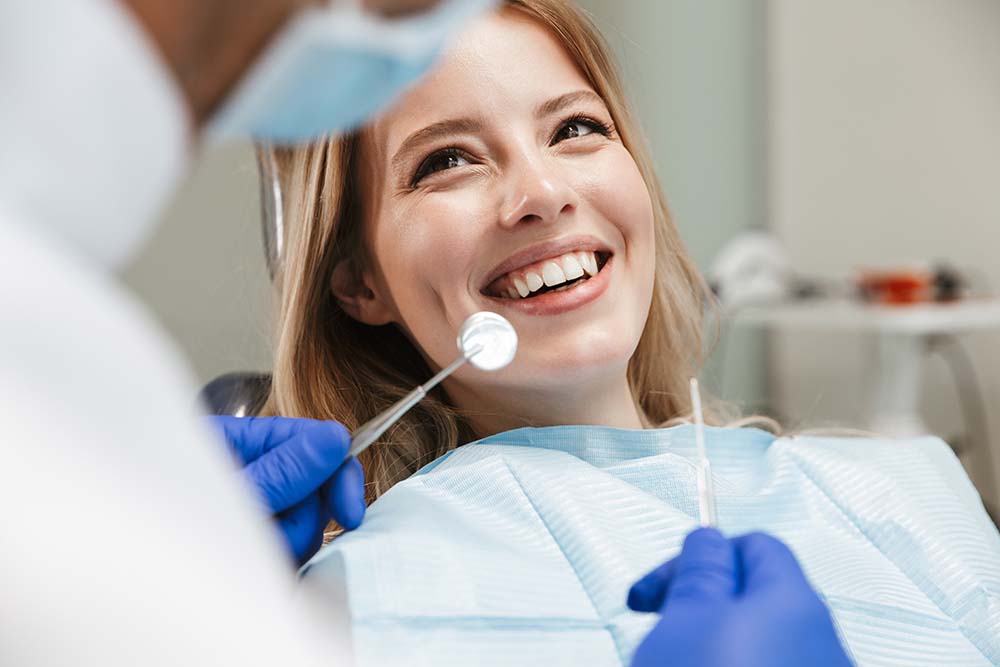 A woman receiving dental care with a smile, surrounded by dental equipment and professionals in blue gowns.