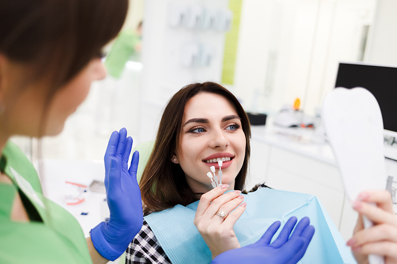A woman sitting in a dental chair with a hygienist performing a cleaning procedure on her teeth.