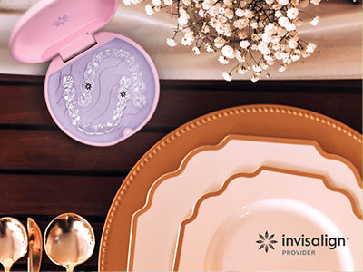The image features a collection of tableware items, including plates, bowls, and a decorative box, arranged on a wooden surface with a pink and white color scheme, set against a backdrop that includes a floral arrangement and a partial view of a product packaging with the text  Invisalign  visible.