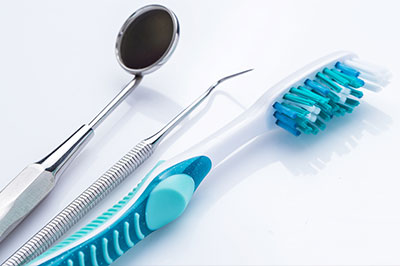 The image displays a collection of dental instruments including toothbrushes and scissors, with a focus on blue-toned items against a white background.