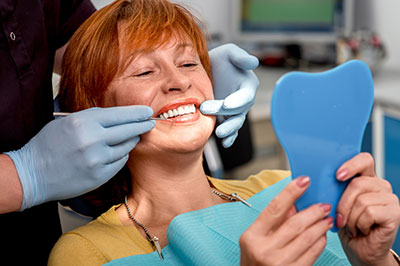 A woman seated at a dental chair, receiving dental care with a blue mouthguard on her teeth, while holding a mirror showing the mouthguard.