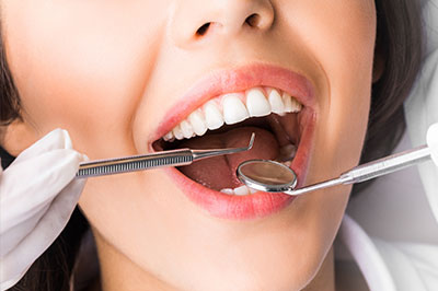 The image shows a woman with an open mouth, receiving dental care from a professional using tools, while wearing gloves and a mask.