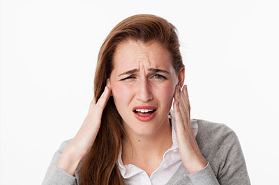 The image shows a woman with her hand on her head, appearing to be in distress or discomfort, with a close-up view emphasizing her facial expression.