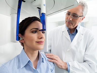 The image features a woman seated in a dental chair, wearing a blue headgear, with her eyes closed, being attended by a dentist who appears to be conducting a dental examination or procedure.