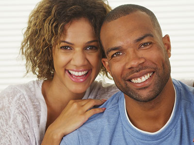 A man and woman smiling at the camera, with the man wearing a short beard and the woman having curly hair.