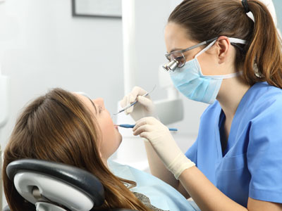 A dental hygienist is performing oral care on a patient while wearing personal protective equipment.