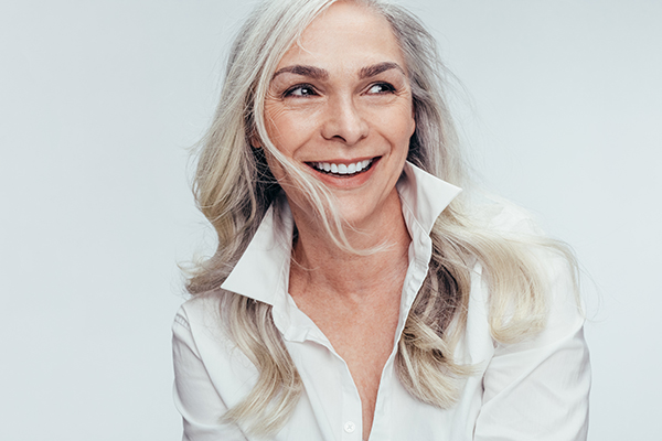 The image shows a woman with short hair smiling at the camera. She has her hair styled upwards and is wearing a white blouse with a collar.