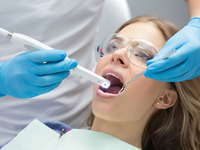 The image depicts a dental professional performing a dental procedure on a patient, with the patient s mouth open and the dental professional using specialized equipment.
