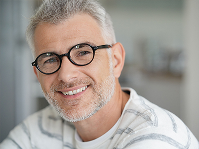 The image shows a man with glasses and a beard smiling at the camera, wearing a white shirt with a patterned design.