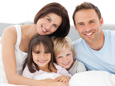 A family of five, including two adults and three children, posing for a photograph with smiles on their faces, set against a white wall.