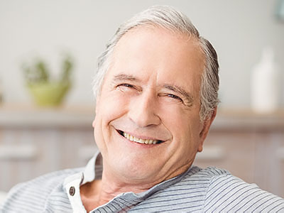 This is an image of an older man with white hair, smiling contentedly while sitting in a chair at home.