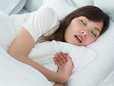 A woman peacefully sleeping with her eyes closed in a cozy bedroom setting.