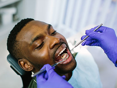 A man receiving dental care with tools being used by a professional in a medical setting.