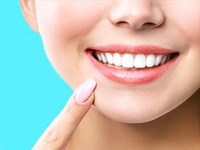 The image shows a close-up of a person s face with a radiant smile, featuring straight white teeth and pink lipstick, against a plain blue background.