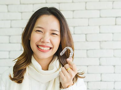 A woman holding up a toothbrush with a smile on her face, next to an image of a smiling man with a toothbrush in his mouth, set against a brick wall background.